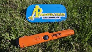 Pinpointer Garrett Pro-Pointer AT orange et noir, tenu dans une main, avec sa pointe de détection et son unique bouton de commande bien visibles.