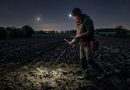 Un prospecteur dans un champ avec son détecteur de métaux, au milieu de la nuit